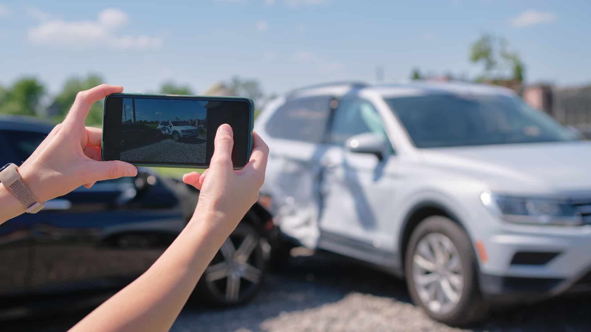 Mani femminili che reggono uno smartphone mentre scattano una foto a due veicoli che si sono urtati.
