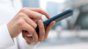 Le mani di una persona mentre reggono uno smartphone e con un dito mettono una firma elettronica.