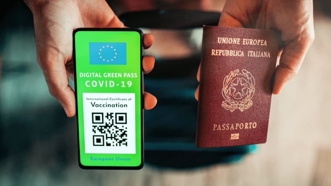 Due mani mostrano uno smartphone col green pass e un passaporto cartaceo.