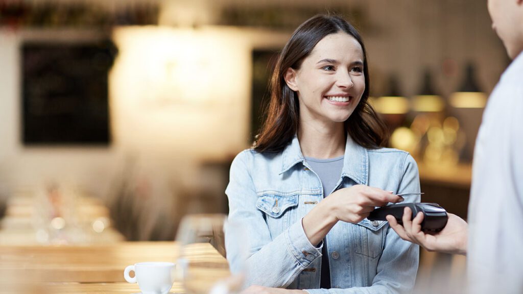 NFC nei sistemi di pagamento, donna al ristorante paga avvicinando la carta al pos