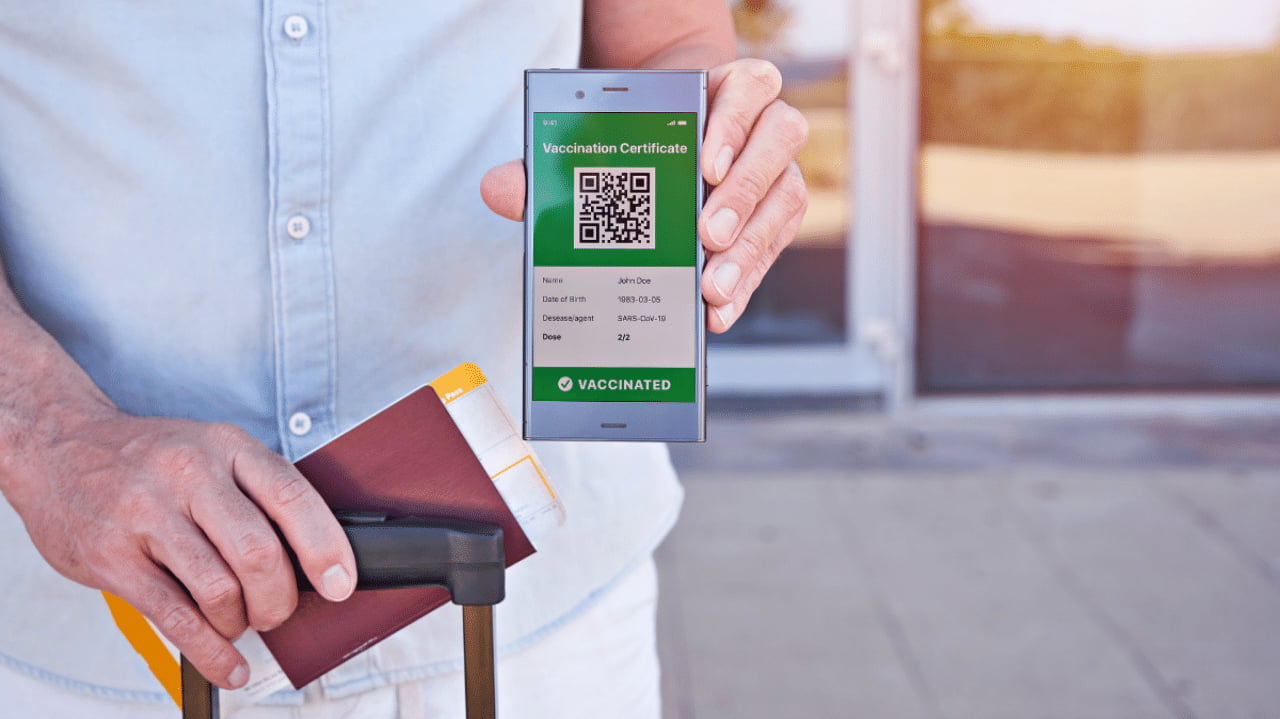 Un viaggiatore con trolley e passaporto mostra il green pass dallo smartphone.