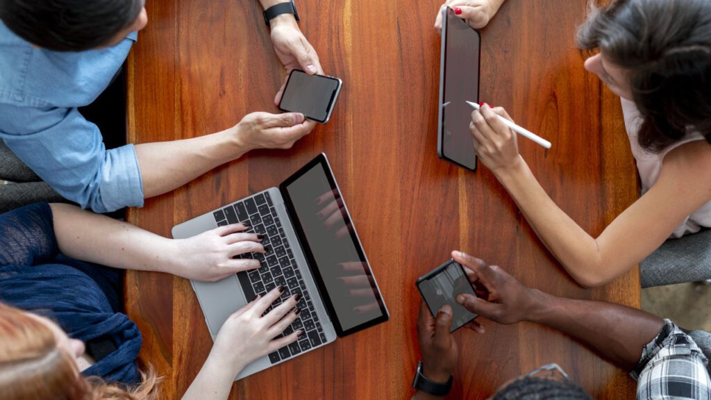 Persone al tavolo con il proprio device usano la piattaforma online per la raccolta firme per i referendum