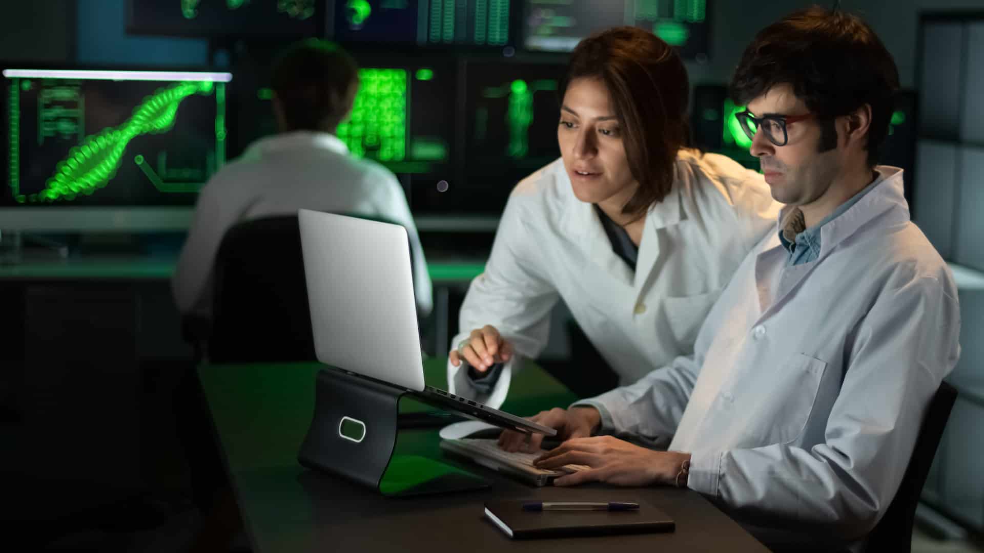 Medici con un portatile, in una sala con vari monitor su cui si vedono grafici e dati.